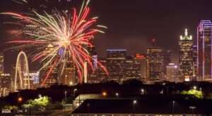 Colorful Fourth of July fireworks burst over the skyline at night, illuminating downtown skyscrapers and city landmarks.