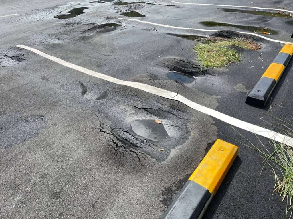 Damaged asphalt parking lot with multiple potholes, standing water, and surface cracking, highlighting the need for pavement repair and maintenance.