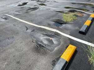 Damaged asphalt parking lot with multiple potholes, standing water, and surface cracking, highlighting the need for pavement repair and maintenance.